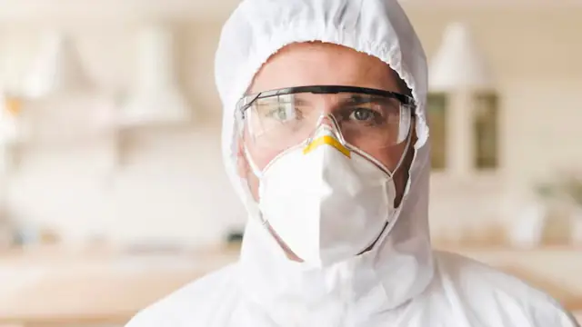 Worker in a white suit, goggles and respirator in a bright room