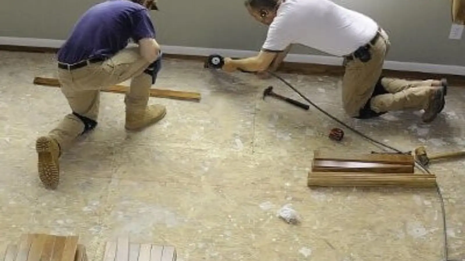 Two workers kneeling on a bare subfloor while repairing water damage
